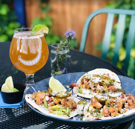 A glass of Wonderland Brewing's beer with some tacos on a patio table.